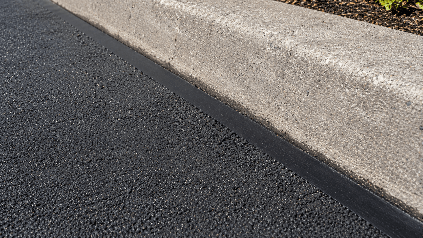 Close-up of a properly sealed asphalt to concrete joint along a commercial parking lot curb
